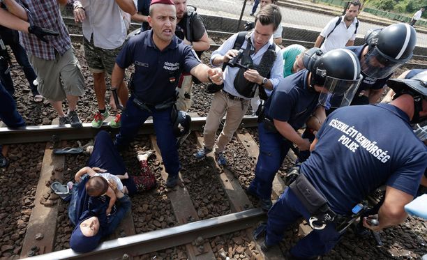 Pakolaisnainen makasi lapsi sylissään rautatiekiskoilla Unkarin Bicskessä. Mies, mahdollisesti hänen aviomiehensä, oli sysännyt hänet siihen hetkeä aiemmin.