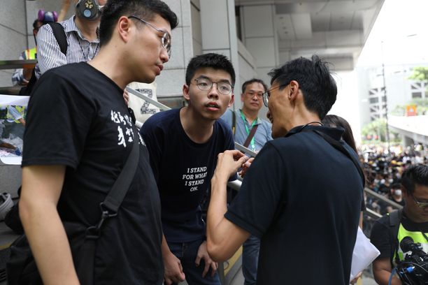 Demokratia-aktivisti Joshua Wong (kesk.) puhui lainsäätäjä Au Nok-hinin (vas.) ja Eddie Chun (oik.) kanssa poliisin päämajan edessä Hong Kongissa tänään 21.6.