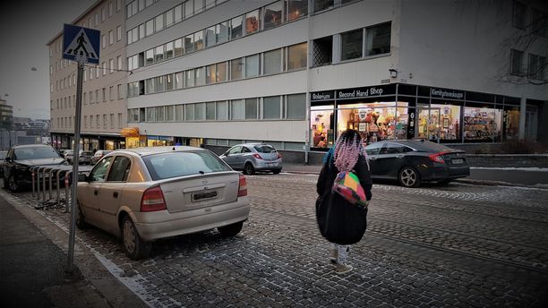 Nuori nainen ylittämässä varoen suojatietä Porthaninkadulla väärin pysäköidyn Opelin kohdalla.
