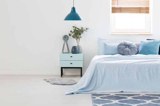 Siniset tekstiilit, matto, valaisin ja yöpöytä luovat uneliaan tunnelman.