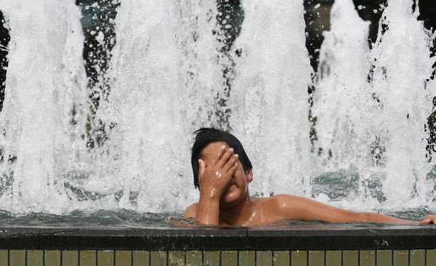 Mies vilvoittaa itseään suihkulähteessä Tokiossa (Arkistokuva). Ennusteiden mukaan päivälämpötilat kipuavat Tokiossa yli + 33 asteen viikonloppuna ja ensi viikon alussa.