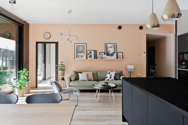 Tässä kodissa olohuoneen trendikäs tunnelma syntyy seinän väristä. Nyt trendikkäitä ovat lämpimät kuparin ja persikan sävyt. Huomaa myös muodikkaat metalliset valaisimet.