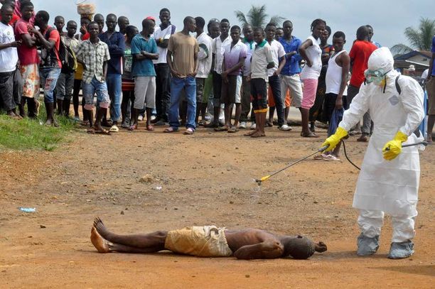 Terveystyöntekijä ruiskutti Liberian pääkaupungissa Monroviassa desinfioivia kemikaaleja vainajaan, jonka epäillään kuolleen Ebolaan.